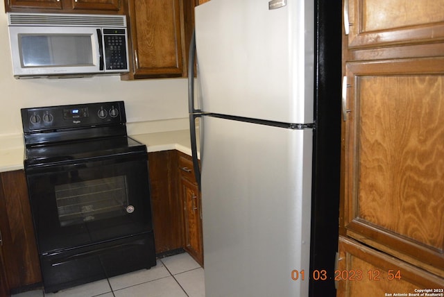4107 Medical Dr Unit 8204, San Antonio, TX 78229 - kitchen with freestanding refrigerator, black electric range oven, stainless steel microwave, light tile patterned floors, and light countertops