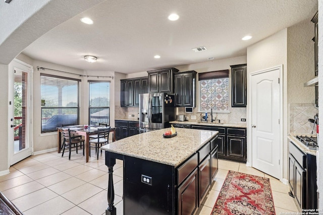 630 Oxalis, San Antonio, TX 78260 - kitchen featuring appliances with stainless steel finishes, light tile patterned floors, dark cabinets, backsplash, and a kitchen island