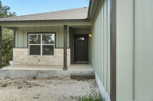 150 Hill Dr, Spring Branch, TX 78070 - view of exterior entry featuring roof with shingles, board and batten siding, covered porch, and stone siding