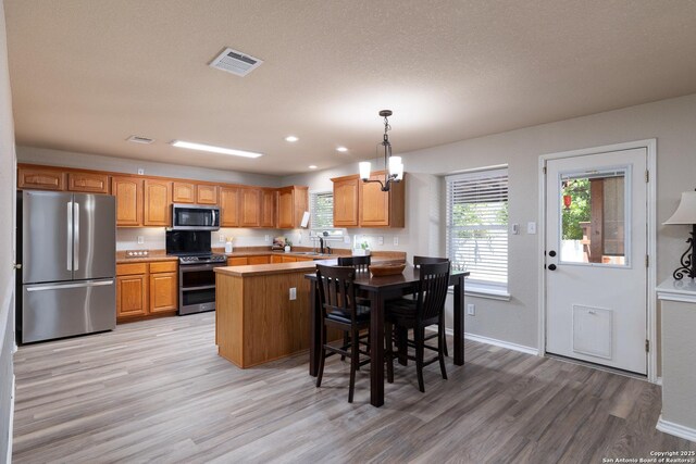 9915 Mustang Isle, San Antonio, TX 78254 - kitchen featuring stainless steel appliances, light wood-style floors, pendant lighting, a peninsula, and a breakfast bar