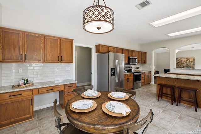 18310 Redwood Path, San Antonio, TX 78259 - kitchen featuring appliances with stainless steel finishes, decorative backsplash, light tile patterned flooring, brown cabinetry, and arched walkways