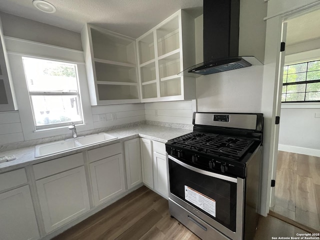 603 Humboldt, San Antonio, TX 78211 - kitchen featuring stainless steel range with gas stovetop, wall chimney exhaust hood, light wood finished floors, light countertops, and white cabinetry
