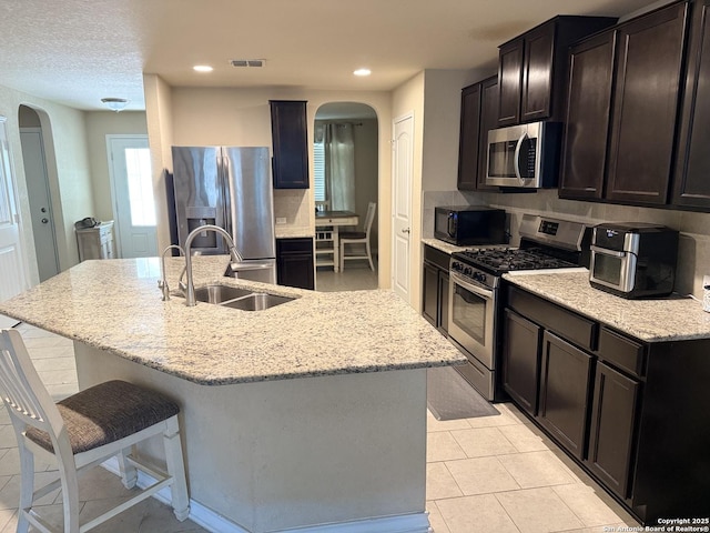 15530 Gray Catbird, San Antonio, TX 78253 - kitchen featuring appliances with stainless steel finishes, arched walkways, light stone countertops, a center island with sink, and a breakfast bar