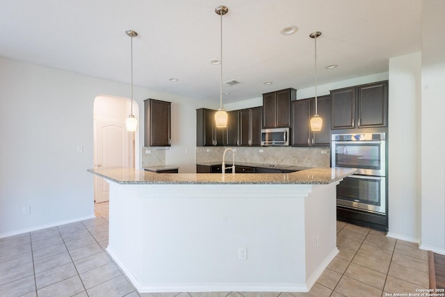 20131 Silver, San Antonio, TX 78259 - kitchen with stainless steel appliances, a center island with sink, decorative backsplash, dark brown cabinetry, and light tile patterned floors