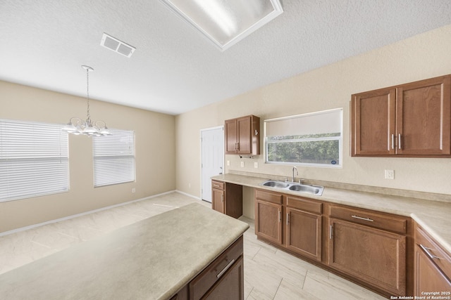 5715 Sendero Spg, San Antonio, TX 78251 - kitchen with decorative light fixtures, a chandelier, brown cabinetry, light countertops, and a textured ceiling