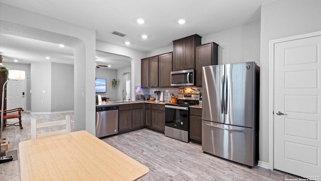 6314 Hibiscus Fls, San Antonio, TX 78218 - kitchen featuring stainless steel appliances, dark brown cabinetry, arched walkways, light wood-style flooring, and decorative backsplash