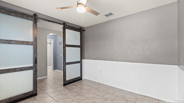 702 Pelican Pt, San Antonio, TX 78221 - unfurnished room featuring arched walkways, a barn door, ceiling fan, a wainscoted wall, and light tile patterned flooring
