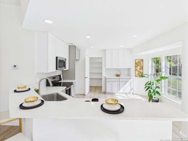 7007 Elk Trl, San Antonio, TX 78244 - kitchen featuring appliances with stainless steel finishes, a peninsula, light wood finished floors, light stone counters, and white cabinetry
