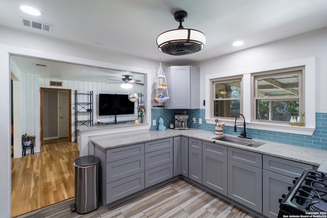 450 Pamela, San Antonio, TX 78223 - kitchen featuring gray cabinetry, a peninsula, backsplash, light stone counters, and range with gas stovetop