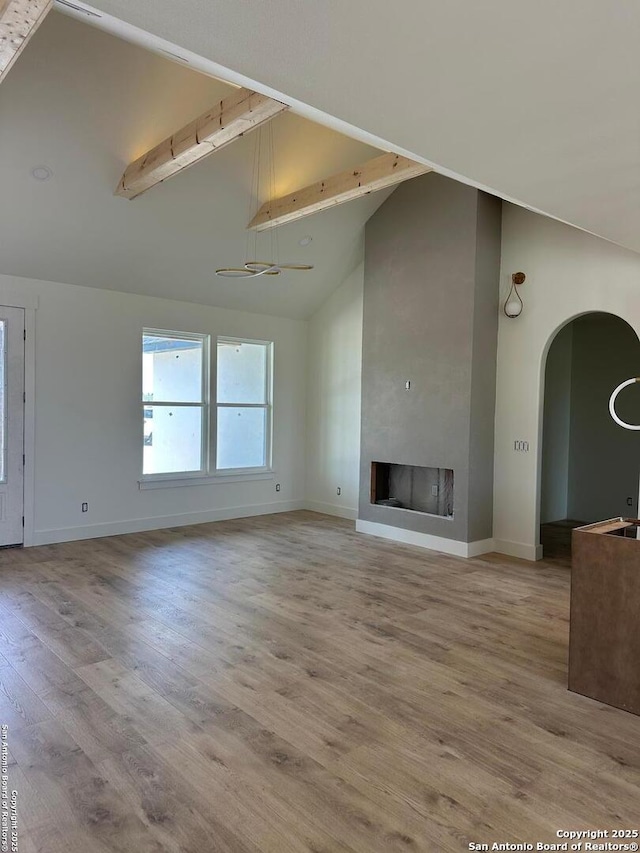 129 Merion Ln, Vernia, TX 78121 - unfurnished living room with beamed ceiling, wood finished floors, arched walkways, high vaulted ceiling, and a large fireplace