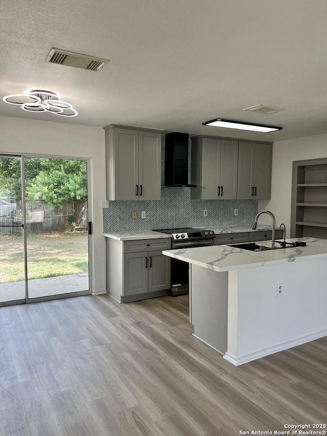 7947 Ruby Mdws, San Antonio, TX 78251 - kitchen with gray cabinetry, stainless steel range with electric stovetop, wall chimney exhaust hood, and light wood-style floors
