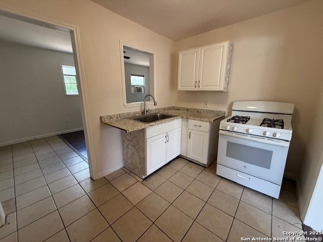 207 Fargo, San Antonio, TX 78220 - kitchen featuring white gas range, white cabinetry, light tile patterned flooring, and light stone counters