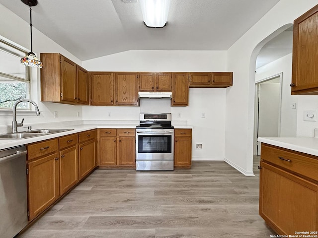 1222 Bobcat Pass, San Antonio, TX 78251 - kitchen featuring appliances with stainless steel finishes, brown cabinetry, under cabinet range hood, arched walkways, and vaulted ceiling