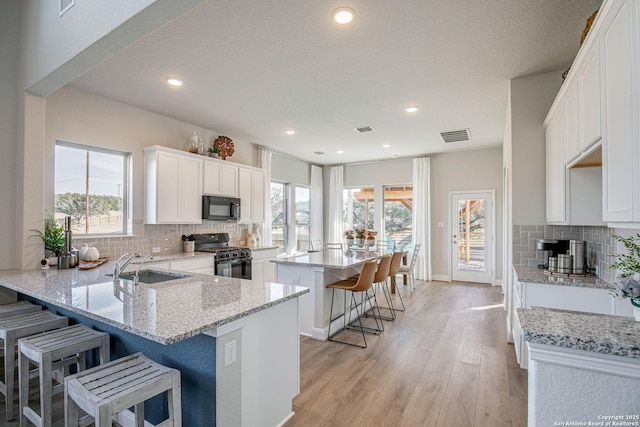 9354 Luke Path, San Antonio, TX 78254 - kitchen with black appliances, a breakfast bar area, decorative backsplash, light stone countertops, and white cabinetry