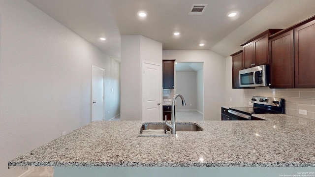 2076 Meadow Pipit, New Braunfels, TX 78130 - kitchen with stainless steel appliances, light stone counters, backsplash, dark brown cabinetry, and a peninsula