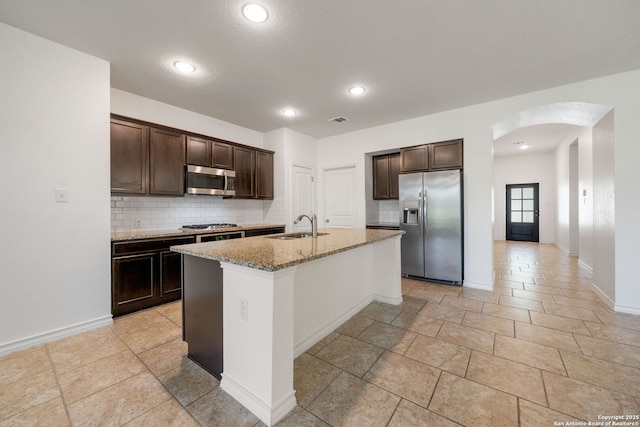 14724 Costa Leon, San Antonio, TX 78245 - kitchen featuring stainless steel appliances, arched walkways, backsplash, dark brown cabinets, and light stone counters