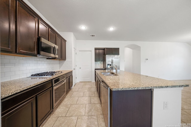14724 Costa Leon, San Antonio, TX 78245 - kitchen featuring appliances with stainless steel finishes, decorative backsplash, an island with sink, light stone countertops, and dark brown cabinetry