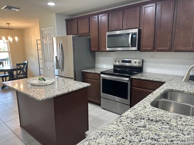 9510 Silveer Mist Way, San Antonio, TX 78254 - kitchen with stainless steel appliances, a chandelier, light tile patterned flooring, tasteful backsplash, and a kitchen island