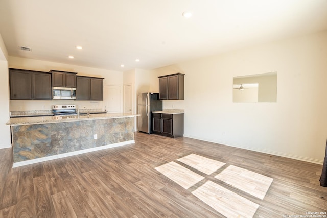 7335 Sharma Vly, San Antonio, TX 78252 - kitchen with appliances with stainless steel finishes, dark brown cabinets, light wood-type flooring, recessed lighting, and a center island with sink