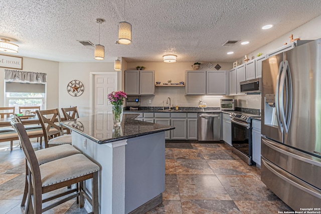 7907 Donshire, Converse, TX 78109 - kitchen featuring appliances with stainless steel finishes, gray cabinets, a breakfast bar area, a textured ceiling, and decorative light fixtures