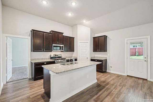 11518 Biddle, San Antonio, TX 78253 - kitchen with stainless steel appliances, wood finished floors, dark brown cabinets, light stone counters, and a kitchen island with sink