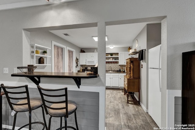 332 W Klein, Seguin, TX 78155 - kitchen featuring a textured wall, dark countertops, white microwave, a breakfast bar, and white cabinets