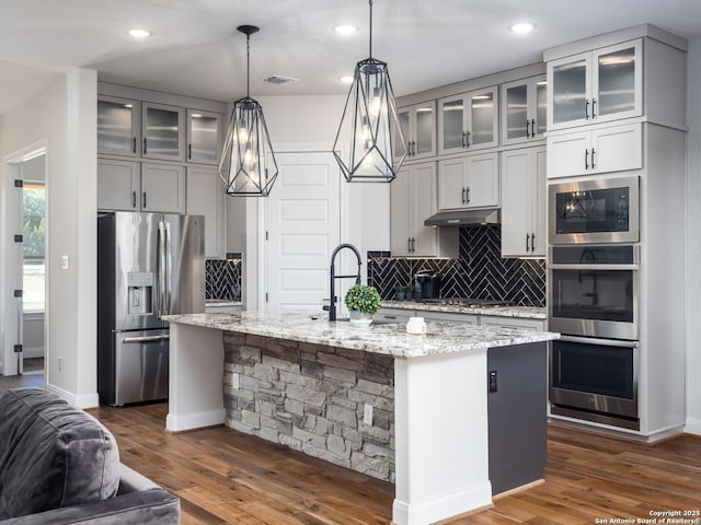 555 Mystic Pkwy, Spring Branch, TX 78070 - kitchen with appliances with stainless steel finishes, decorative backsplash, light stone countertops, dark wood finished floors, and a kitchen island with sink