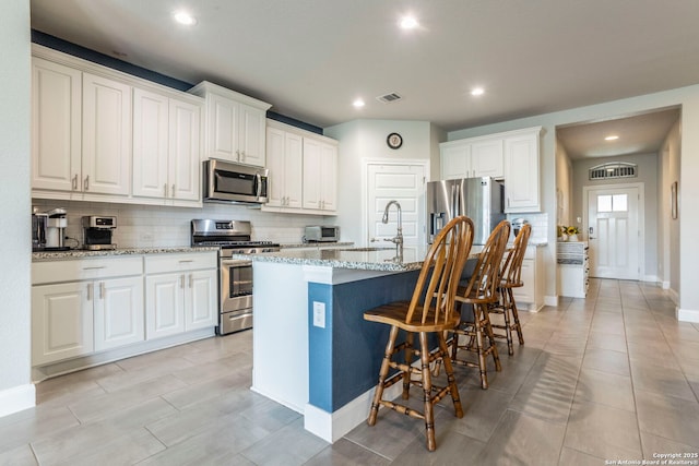 13822 Greater Straw, San Antonio, TX 78254 - kitchen with stainless steel appliances, decorative backsplash, a kitchen bar, light stone countertops, and a kitchen island with sink