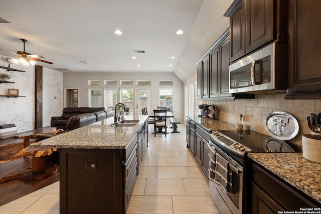 2129 Rustling Way, Seguin, TX 78155 - kitchen with stainless steel appliances, decorative backsplash, light stone counters, a center island with sink, and dark brown cabinets