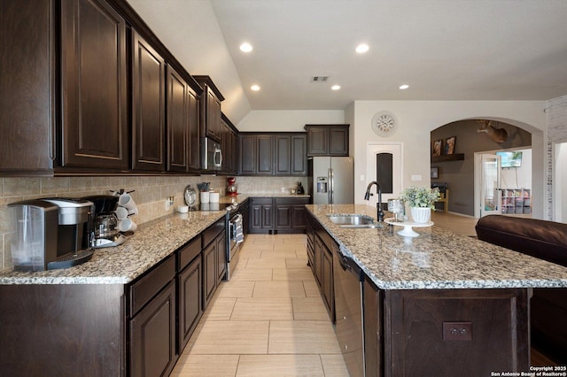2129 Rustling Way, Seguin, TX 78155 - kitchen featuring appliances with stainless steel finishes, decorative backsplash, dark brown cabinets, light stone counters, and arched walkways