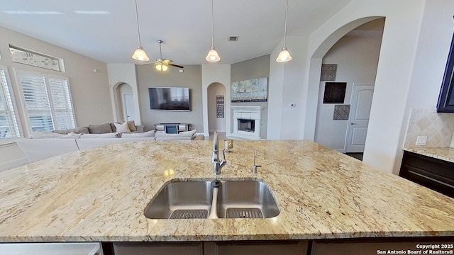3822 Cordoba Crk, San Antonio, TX 78259 - kitchen with a fireplace, ceiling fan, a center island with sink, open floor plan, and light stone counters