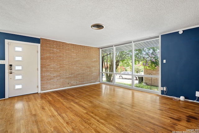 250 Maplewood, San Antonio, TX 78216 - unfurnished room featuring a textured ceiling, wood finished floors, expansive windows, and brick wall
