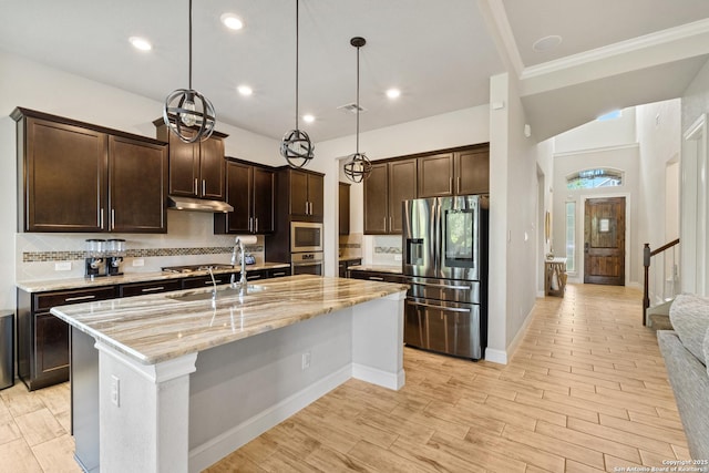 11910 Wilby, San Antonio, TX 78253 - kitchen featuring appliances with stainless steel finishes, under cabinet range hood, dark brown cabinets, light stone counters, and a kitchen island with sink