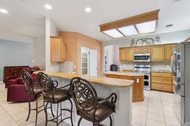 127 Sunflower Ln, San Antonio, TX 78213 - kitchen featuring appliances with stainless steel finishes, a peninsula, tasteful backsplash, light tile patterned floors, and a kitchen bar