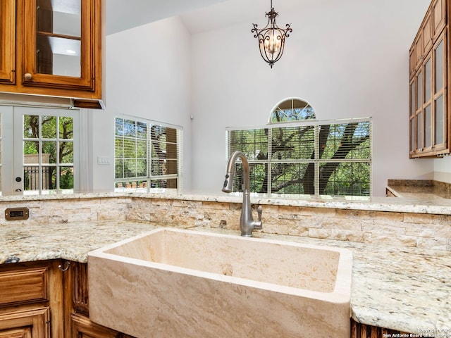 6 De Zavala, Shavano Park, TX 78231 - kitchen with brown cabinetry, light stone counters, glass insert cabinets, a high ceiling, and decorative light fixtures