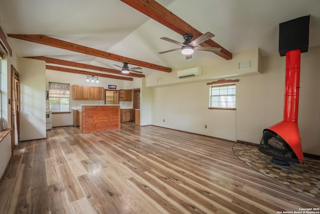 9071 Fm 725, Mcqueeney, TX 78123 - unfurnished living room featuring a wood stove, an AC wall unit, ceiling fan, light wood-type flooring, and healthy amount of natural light