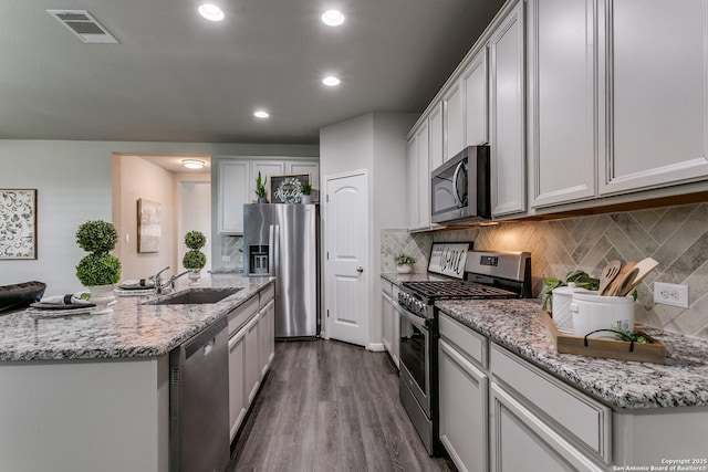6838 Dashmoor Crk, San Antonio, TX 78244 - kitchen with appliances with stainless steel finishes, a center island with sink, tasteful backsplash, dark wood-type flooring, and light stone countertops