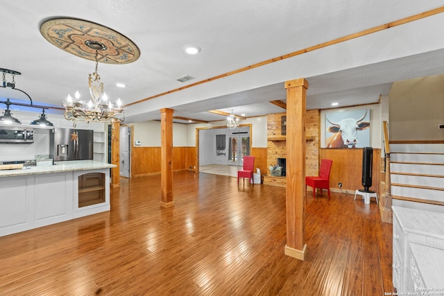 6033 Cammie, Leon Valley, TX 78238 - unfurnished living room with wooden walls, wainscoting, a chandelier, decorative columns, and wood finished floors