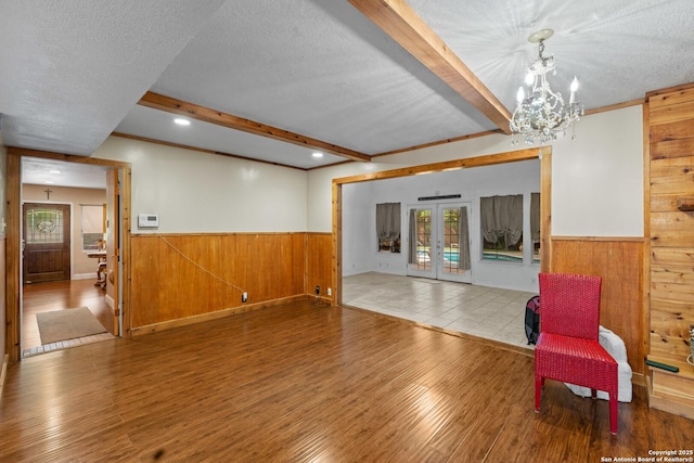 6033 Cammie, Leon Valley, TX 78238 - unfurnished living room featuring french doors, a textured ceiling, wainscoting, wood walls, and beam ceiling