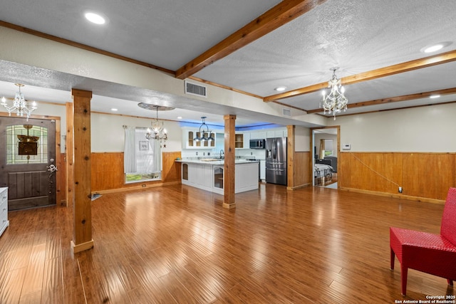 6033 Cammie, Leon Valley, TX 78238 - unfurnished living room featuring a chandelier, a wainscoted wall, a textured ceiling, beam ceiling, and wood walls