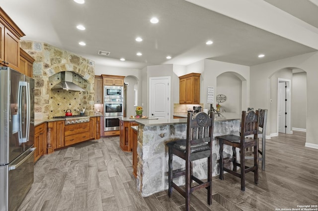 1117 Provence Pl, New Braunfels, TX 78132 - kitchen featuring appliances with stainless steel finishes, wall chimney exhaust hood, arched walkways, recessed lighting, and tasteful backsplash
