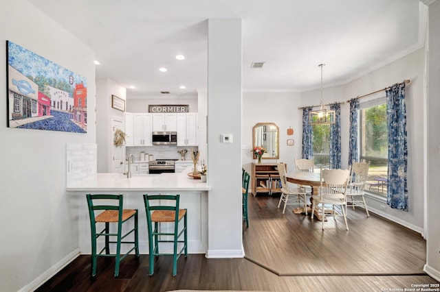 15315 Flying Cir, San Antonio, TX 78023 - kitchen featuring stainless steel appliances, dark wood-type flooring, tasteful backsplash, white cabinets, and a kitchen breakfast bar
