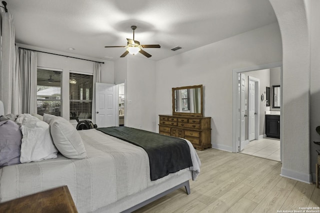 10657 Foxen Way, Helotes, TX 78023 - bedroom featuring light wood-type flooring, arched walkways, ensuite bath, and a ceiling fan