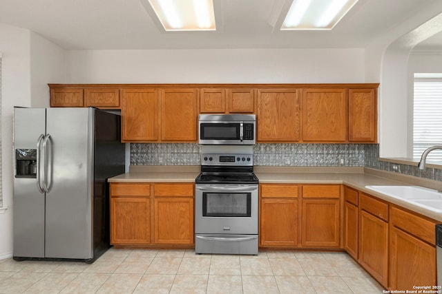 665 La Bahia Loop, New Braunfels, TX 78132 - kitchen with appliances with stainless steel finishes, brown cabinets, backsplash, light countertops, and light tile patterned floors