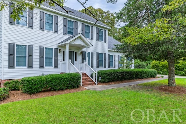 colonial inspired home with roof with shingles and a front yard