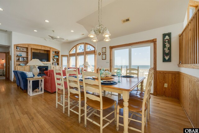 dining space with wainscoting, a fireplace, light wood-style flooring, and a healthy amount of sunlight