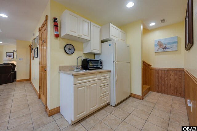 kitchen featuring light tile patterned floors, white cabinets, light countertops, and freestanding refrigerator