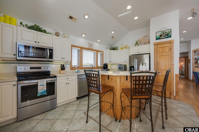 kitchen with visible vents, light countertops, vaulted ceiling, stainless steel appliances, and white cabinetry