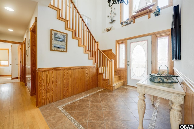 entryway featuring wooden walls, a wainscoted wall, stairs, recessed lighting, and a towering ceiling