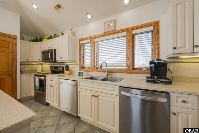 kitchen with a sink, decorative backsplash, light countertops, vaulted ceiling, and stainless steel appliances